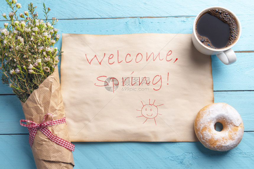 古老的纸上面一张蓝色的桌子上面写着欢迎的春季贺词手写一束白花和带咖啡甜圈的早餐图片