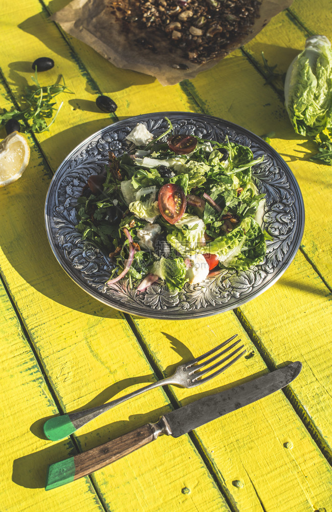 绿色沙拉配有蓝宝石小奶酪橄榄西红柿黄瓜洋葱以及旧金属板古老的黄木桌天然阳光健康食物和饮的概念图片