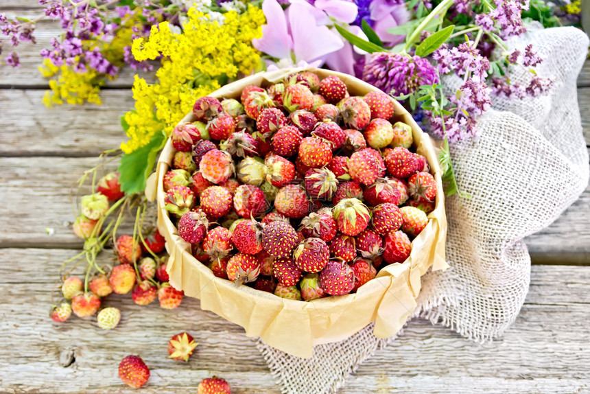 在树皮箱里放着野生成熟的草莓上面有纸卷毛和野花放在旧木板的背景上图片