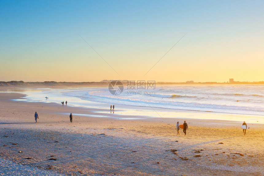 人冲浪者在日落时走海滩上图片