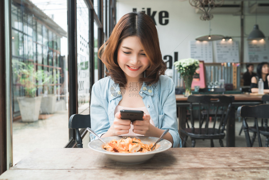 一位年轻女子在智能手机上拍摄意大利面条食品图片