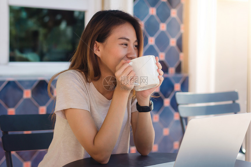 身着智能散装服的亚洲年轻女坐在咖啡馆时用笔记本电脑发送子邮件和喝咖啡生活方式上的妇女交流和从事咖啡店概念方面的工作图片