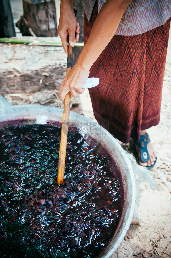 老太婆用竹棍在大锅里搅丝线在泰国布里拉姆染色丝绸的过程图片