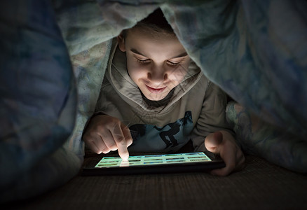 儿童在床上微笑着看平板电脑背景图片