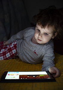 儿童在床上微笑着看平板电脑图片