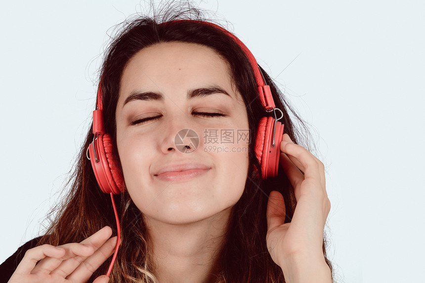 年轻美女在演播室里听着有红耳机的音乐图片