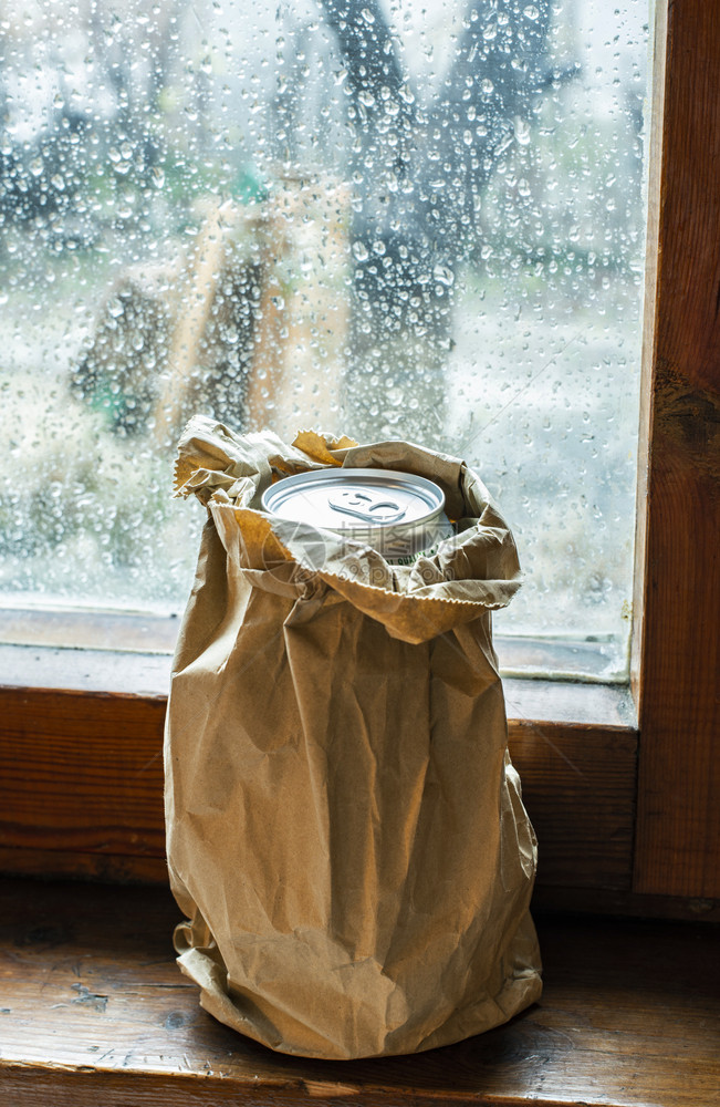 在雨天放窗户的棕色包装纸上有酒精的瓶有皱纹的纸包藏在上的瓶装酒精隐形饮和酗的概念图片