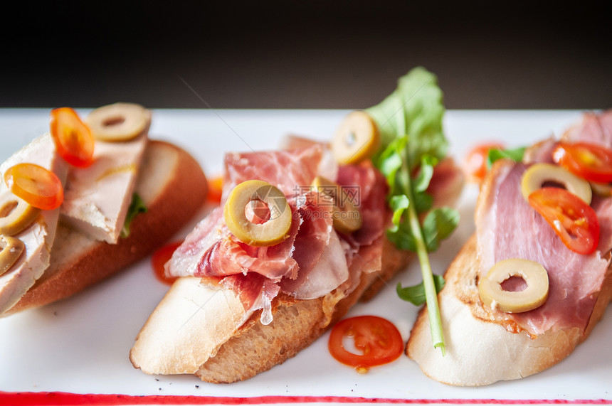 意大利语开胃菜卡帕西奥面包鹅毛草和橄榄马哈姆熏鸭面包和白盘红莓酱图片