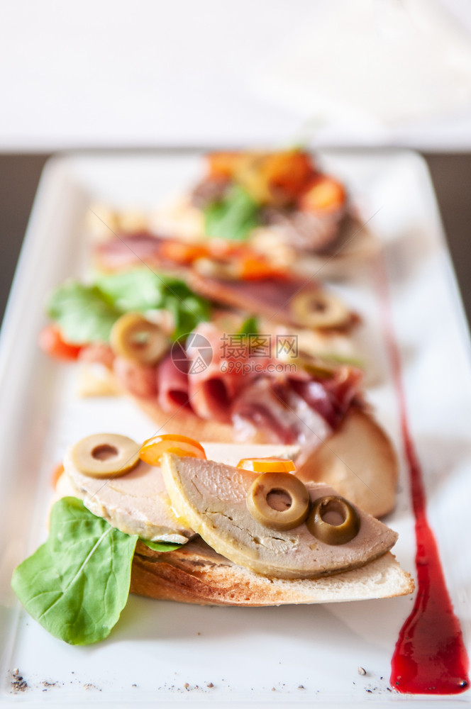 意大利语开胃菜卡帕西奥面包鹅毛草和橄榄马哈姆熏鸭面包和白盘红莓酱图片