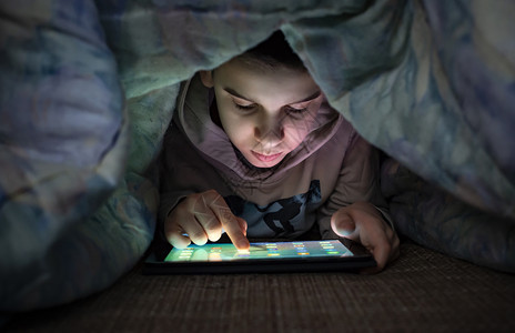 儿童在床上微笑着看平板电脑背景图片