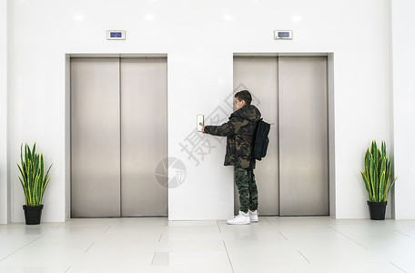 白色运动鞋男孩叫电梯白色当代建筑内部花盆和白色墙上的花朵金属电梯门背景图片