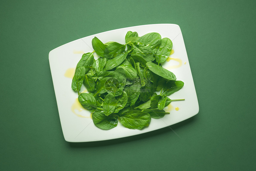 绿色的青小菠菜叶在绿色桌上的白盘子图片