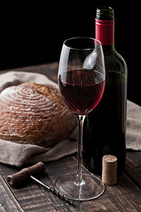 一杯红葡萄酒和瓶配有新鲜面包在木制桌上的厨房里装有旧木制餐桌图片