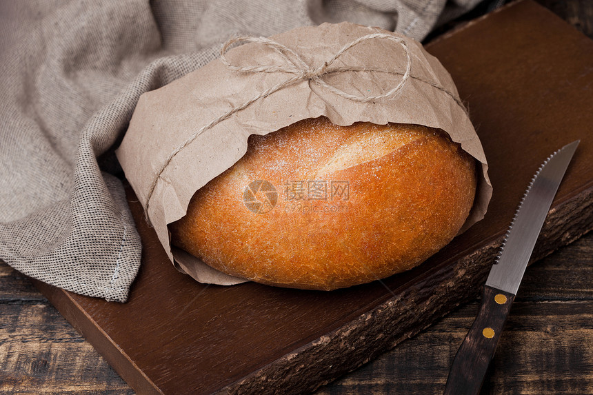 配有厨房毛巾和木砍板上刀子的新鲜烤面包图片