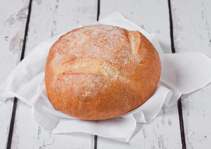 圆白面包配有厨房毛巾和白木板上小麦的新鲜烤面包背景