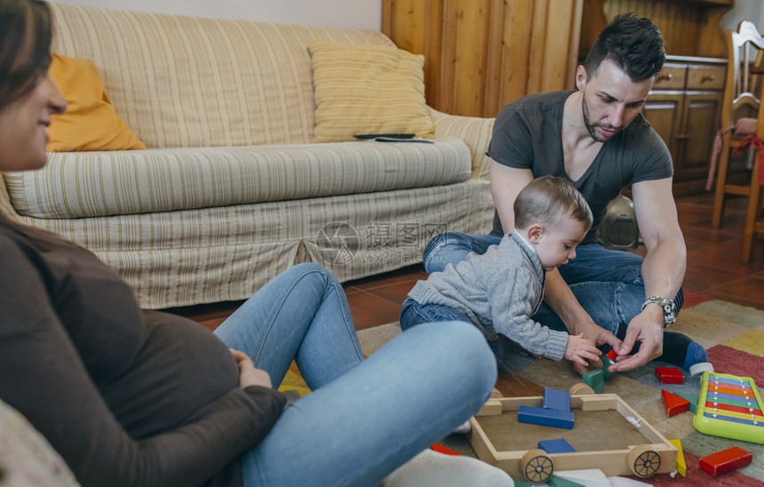 一家三口坐在地毯上母亲看着丈夫陪小宝宝玩积木图片