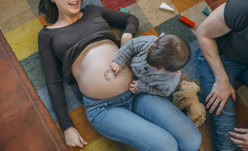 小男孩在他怀孕母亲的肚子蹒跚学步的孩子挠他的肚子图片