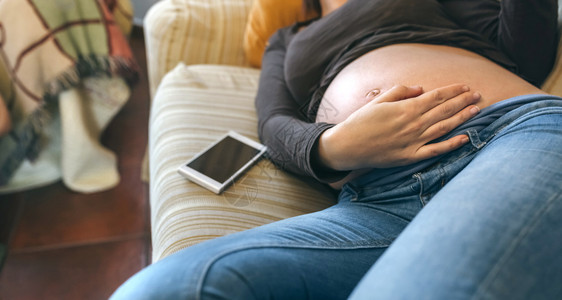 孕妇躺在沙发上抚摸她的肚子图片