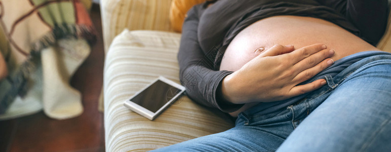 躺在沙发上的孕妇抚摸她的肚子图片