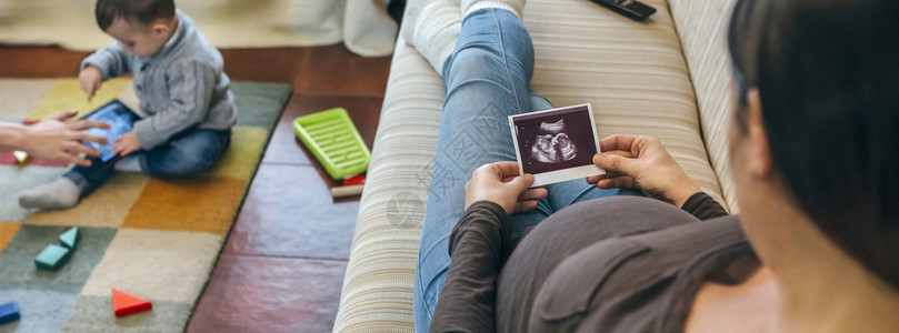 孕妇妈妈看着她的新婴儿超声波而哥却在玩耍图片