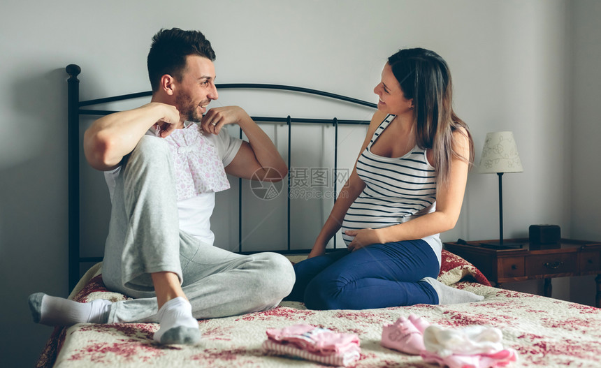 年轻人和他怀孕的妻子为婴儿选择衣服图片