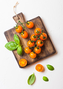 葡萄藤上的有机樱桃橙红番茄白色背景的切肉板上有巴西尔图片