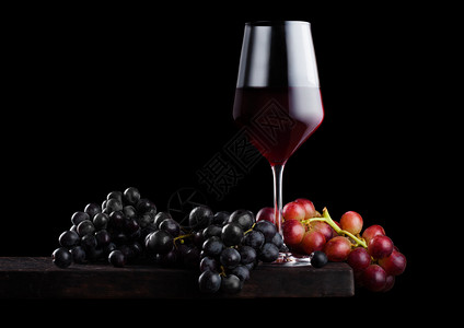 黑色背景的木板上盛着深红葡萄的酒背景图片