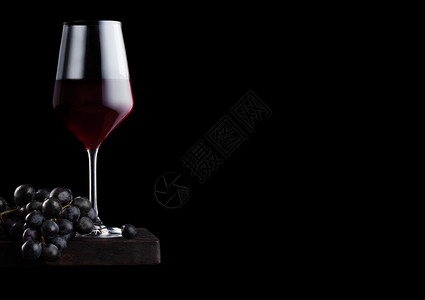 黑色背景的木板上装着深葡萄的优雅红酒杯背景图片