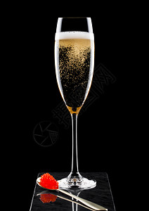 优雅的黄色香槟杯子黑大理石板上的金子勺配红色的鱼酱图片