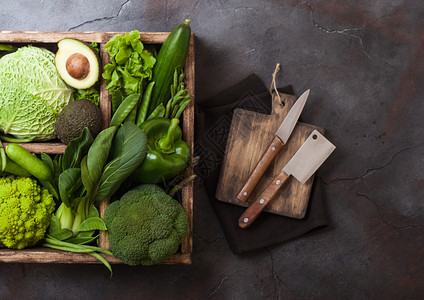 黑石背景的木箱中各种绿色的有机生蔬菜鳄梨卷心菜花椰和黄瓜配有剪断的豆子和用刀砍板背景图片