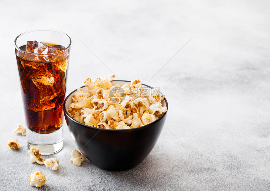 一杯可乐苏打饮料与冰块和黑碗爆米花零食在石器厨房背景图片