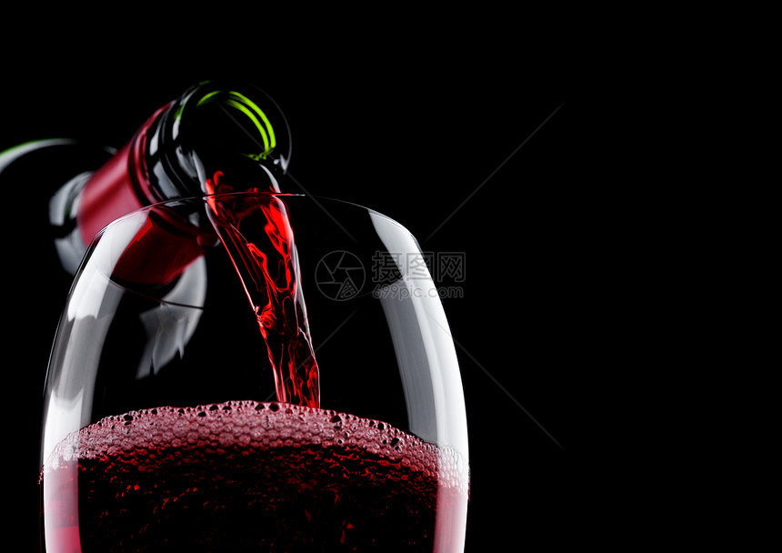 将红酒从瓶子倒到玻璃在黑色背景上隔绝图片