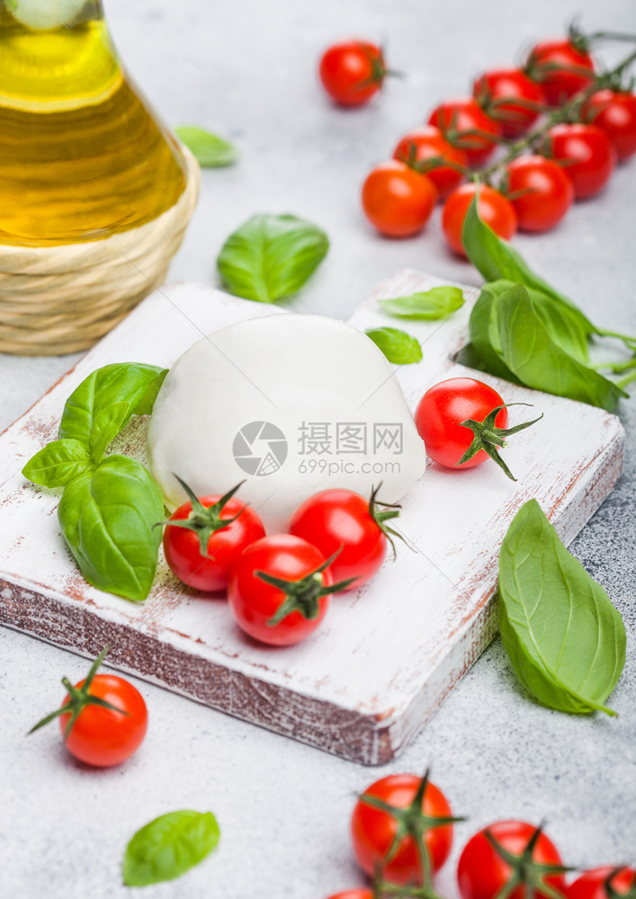 在老式切削板上用番茄和叶在石头厨房背景上加橄榄油图片