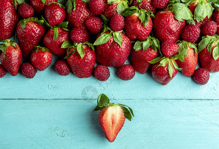 将草莓切片和一堆新鲜草莓放在蓝色木制桌子上图片