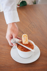 在白杯中用里长针饼干或沙维亚迪做意大利提拉米苏的侍者手图片