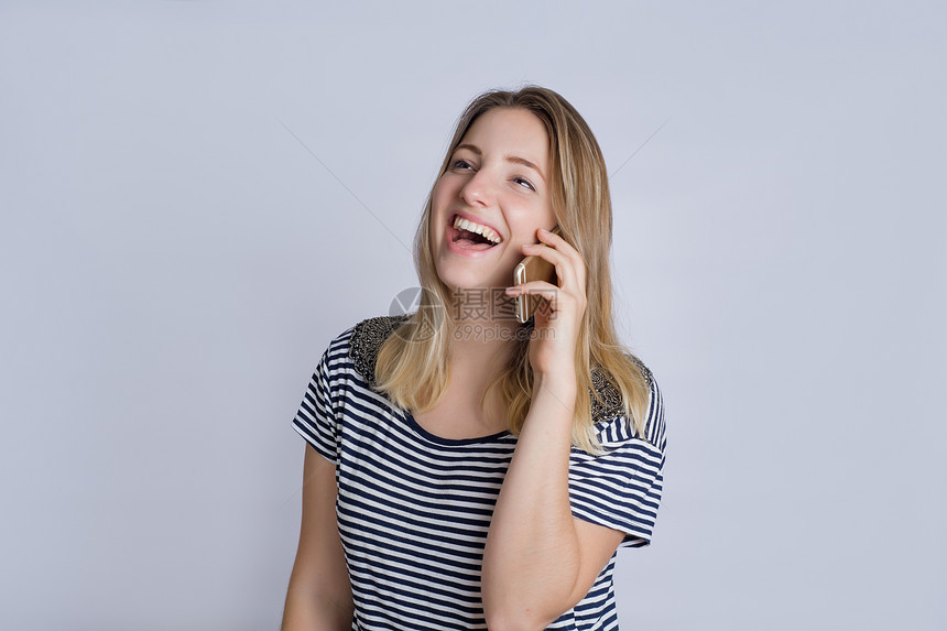 快乐的年轻女子在工作室通过电话交谈的肖像以灰色背景被孤立图片