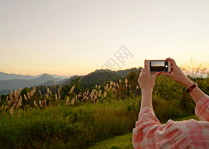 在美丽的山景下年轻女士用手机拍照图片