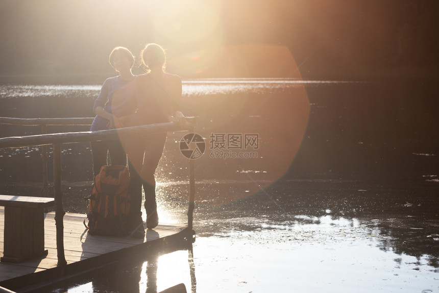 母亲和女儿在山湖的探亲者日落时站在码头上图片