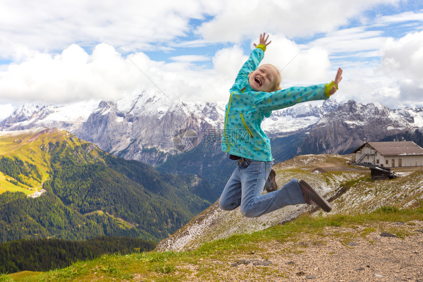 快乐的女童徒步旅行者跳到山上花朵意大利图片