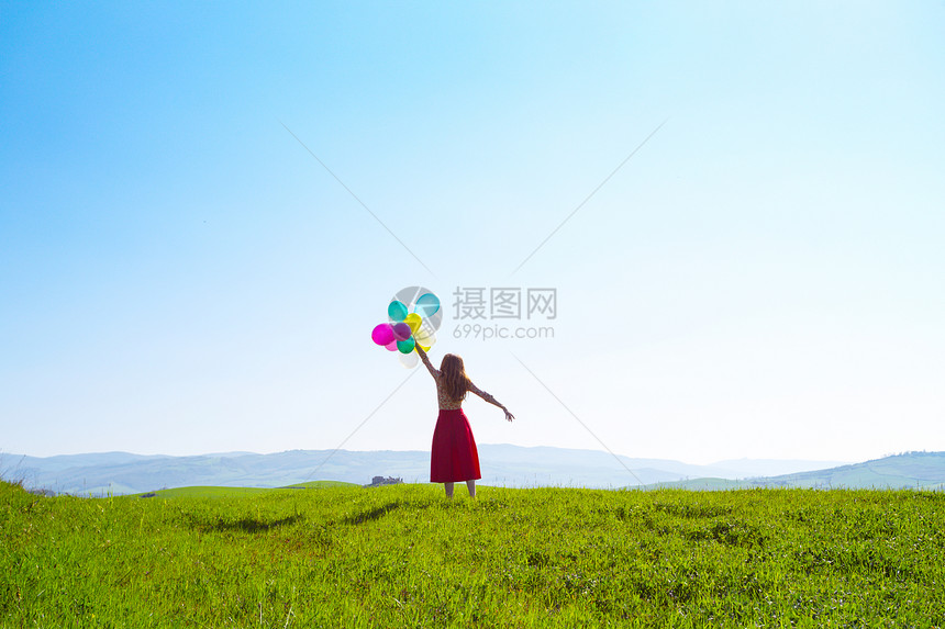 在草地上快乐的女孩带着多彩的气球在蓝天和绿草地上图片