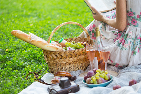 女孩坐在野餐篮子和面包葡萄酒眼镜和卷饼旁看书的女孩图片