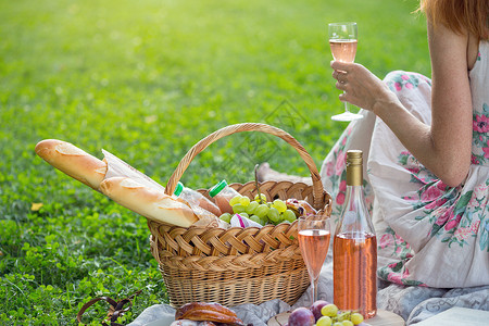 女孩喝杯酒靠近野餐篮子和面包葡萄酒眼镜和面包卷图片