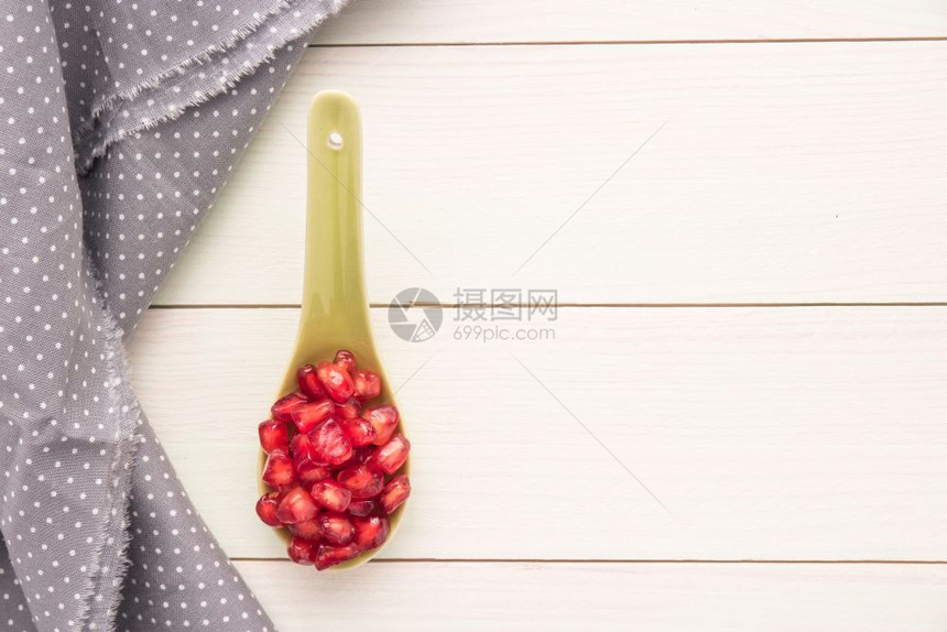 陶瓷勺上红熟皮石榴的种子生木板背景带有Polka点织物顶视图复制空间图片