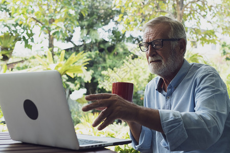 老人在阳台上喝咖啡时不忘看笔记本电脑图片