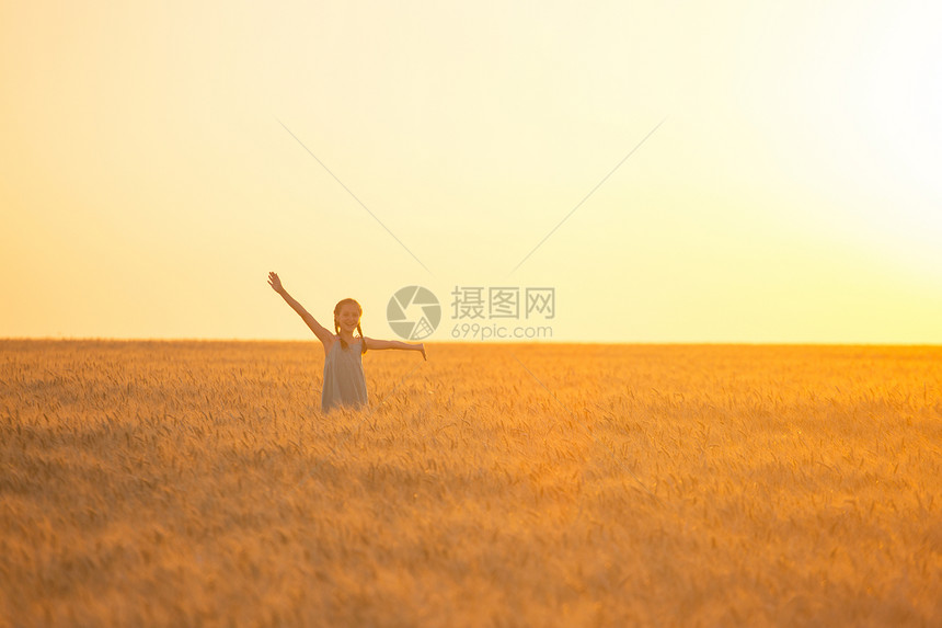 日落时年轻女孩在小麦田上欢乐图片