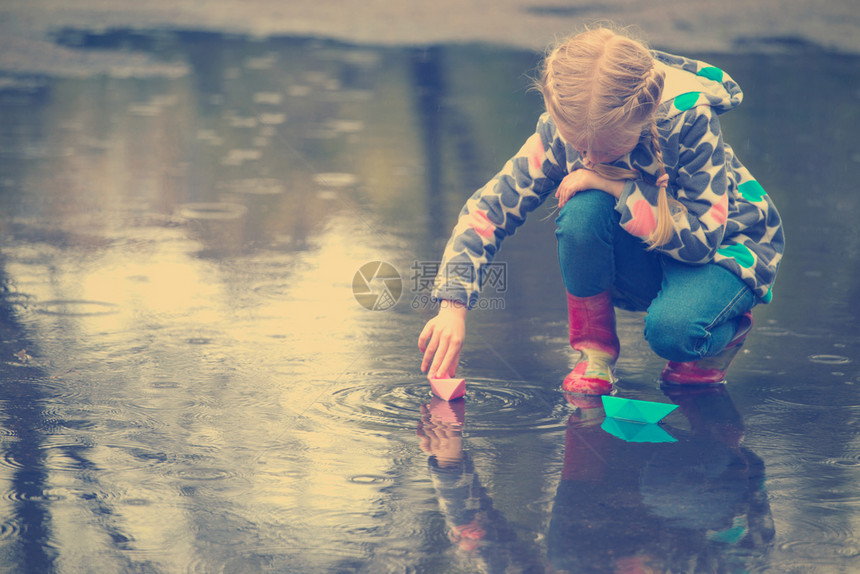 女孩雨中的水坑里玩纸船图片