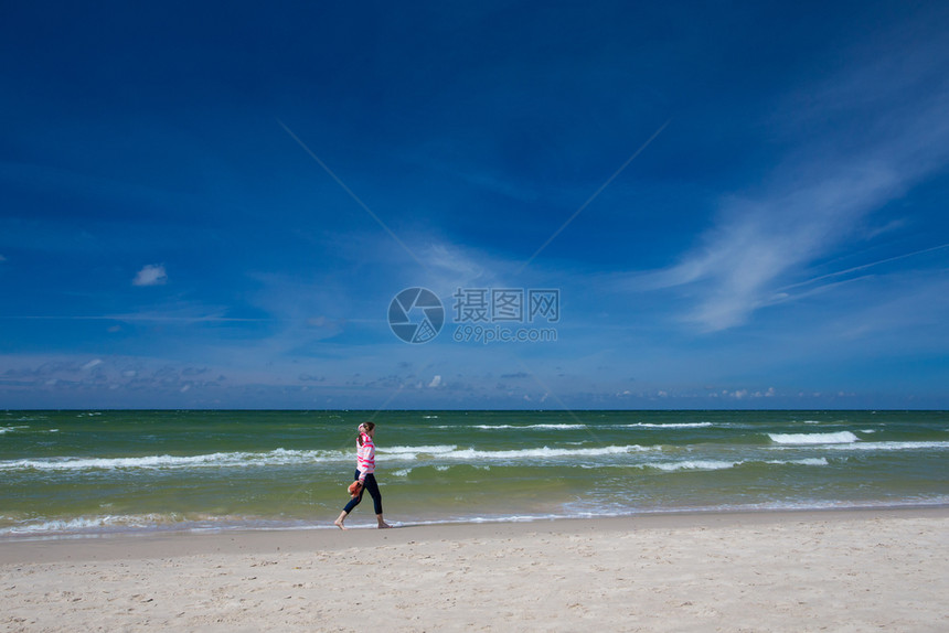 在阳光明媚的风天女孩在空海滩上行走图片
