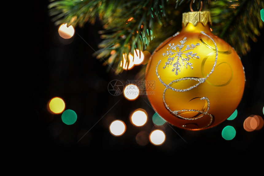 黄色圣诞舞会挂在黑色背景的圣诞树枝上带多色布基的黑背景上图片