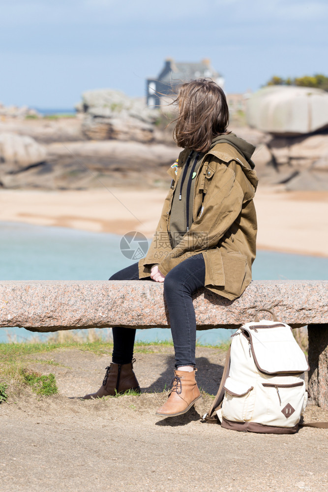 女孩旅行者坐在靠近海边和岸的长凳上在布列塔尼的Trigastel图片