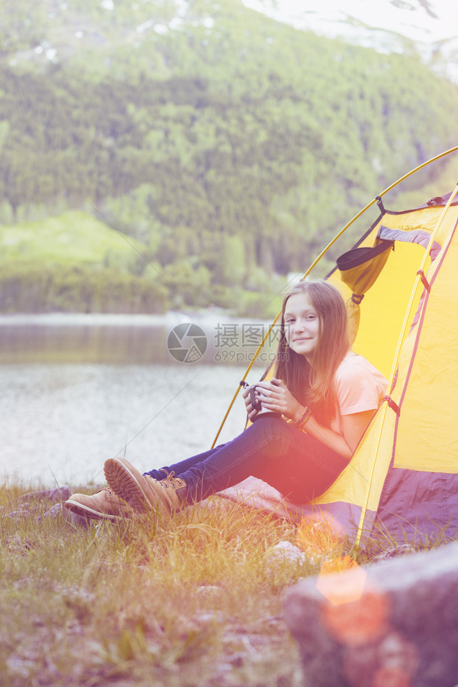 女孩在帐篷里微笑的徒步女孩并在背景中拿着一个杯山图片
